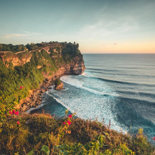 Overview panorama ocean shore, cliff. Sunset. Bali. Overwhelmed scene the flower and green-capped vertical cliff over the Indian ocean. South of Bali island, Pura Luhur Uluwatu Temple. Indonesia.